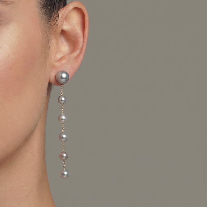 Close-up of a person wearing pearl drop earrings against a neutral background